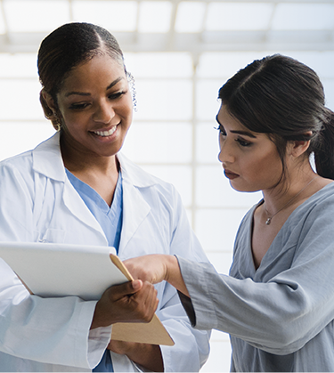 Actor portrayals of female doctor talking with a female patient pointing to clipboard